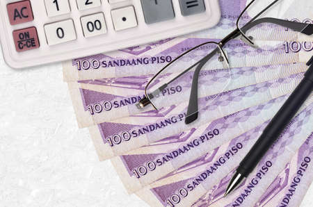 100 Philippine piso bills fan and calculator with glasses and pen. Business loan or tax payment...