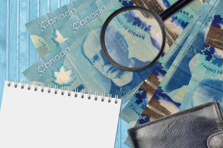 5 Canadian dollars bills and magnifying glass with black purse and notepad. Concept of counterfeit money. Search for differences in details on money bills to detect fake moneyの写真素材