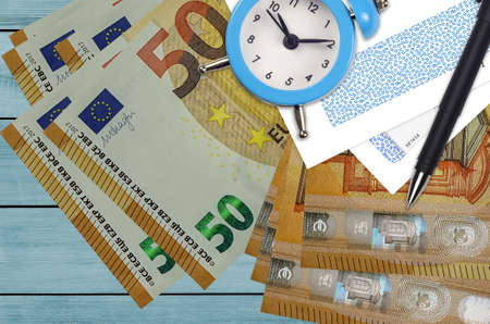 50 euro bills and alarm clock with pen and envelopes. Tax season concept, payment deadline for...