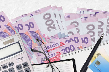 200 Ukrainian hryvnias bills and calculator with glasses and pen. Tax payment season concept or investment solutions. Financial planning or accountant paperworkの写真素材