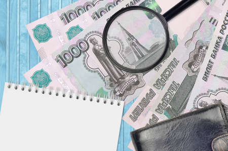 1000 russian rubles bills and magnifying glass with black purse and notepad. Concept of counterfeit money. Search for differences in details on money bills to detect fake moneyの写真素材