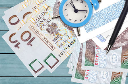 10 Polish zloty bills and alarm clock with pen and envelopes. Tax season concept, payment deadline...