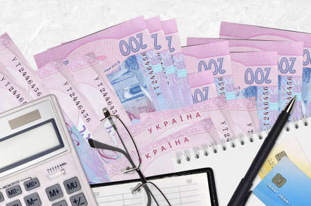 200 Ukrainian hryvnias bills and calculator with glasses and pen. Tax payment season concept or...
