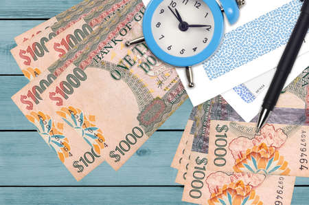 1000 Guyanese dollars bills and alarm clock with pen and envelopes. Tax season concept, payment deadline for credit or loan. Financial operations using postal service. Quick money transferの写真素材