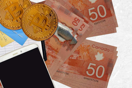 50 Canadian dollars bills and golden bitcoins with smartphone and credit cards. Cryptocurrency...