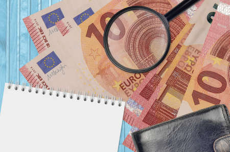 10 euro bills and magnifying glass with black purse and notepad. Concept of counterfeit money....