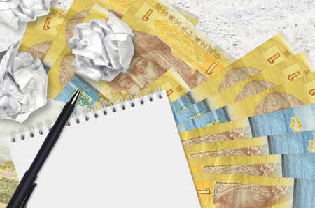 1 Ukrainian hryvnia bills and balls of crumpled paper with notepad. Bad ideas or less of inspiration concept. Searching ideas for investmentの写真素材