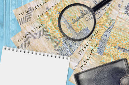 25 Egyptian piastres bills and magnifying glass with black purse and notepad. Concept of counterfeit money. Search for differences in details on money bills to detect fake moneyの写真素材