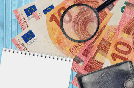 10 euro bills and magnifying glass with black purse and notepad. Concept of counterfeit money. Search for differences in details on money bills to detect fake moneyの写真素材