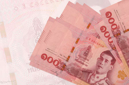 100 Thai baht bills lies in stack on background of big semi-transparent banknote. Abstract...