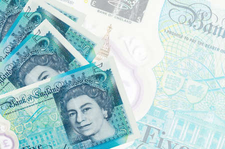5 British pounds bills lies in stack on background of big semi-transparent banknote. Abstract...