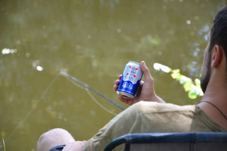 KHARKOV, UKRAINE - AUGUST 22 2020: Young man holds 1664 Kronenbourg Blanc beer can outdoors during fishing. 1664 Blanc is the wheat beer from the French brewery Kronenbourg exported worldwideのeditorial素材
