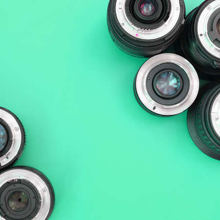 Several photographic lenses lie on a bright turquoise background. Space for text
