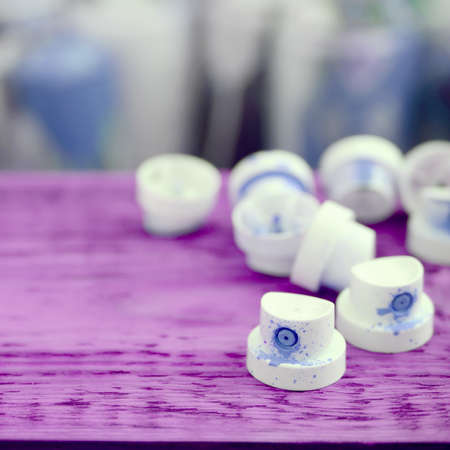 The soiled blue nozzles from the paint sprayer lies on a purple plank on a background of a many dirty spray cans for graffiti paintingの写真素材