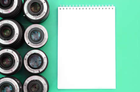 Several photographic lenses and white notebook lie on a bright turquoise background. Space for textの写真素材