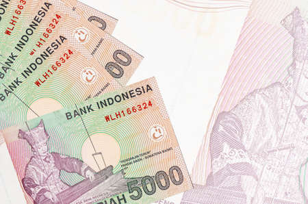 5000 Indonesian rupiah bills lies in stack on background of big semi-transparent banknote. Abstract...