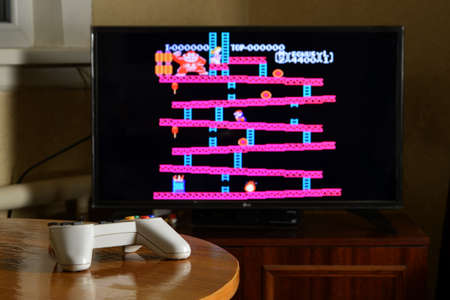 KHARKOV, UKRAINE - NOVEMBER 12, 2020: Dendy video game controller on table with Donkey Kong game on big displayのeditorial素材