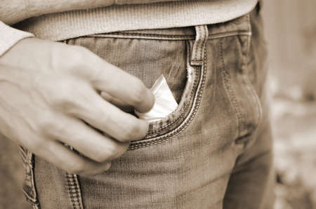 Male hand retrieving drug packet our of blue jean pocket with copy space on abandoned building background. Drug dealing concept. Narcotic addiction problemsの写真素材