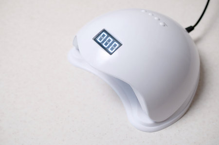 UV LED nail lamp for curing process by gel method lies on white table. Infrared induction helps to dry and cure nails quicklyの写真素材