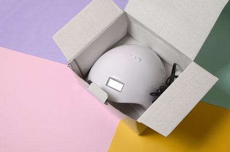 Unboxing of new UV LED nail lamp for curing process by gel method. Cardboard box on pastel multi...