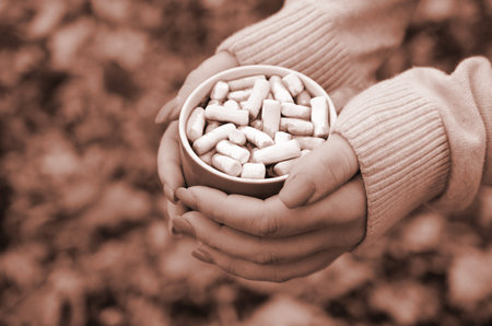Woman wearing white sweater in their hands holding a big coffee cup in a relaxed mood on foliage backgroundの写真素材