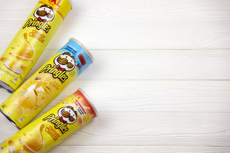KHARKOV, UKRAINE - NOVEMBER 23, 2020: Pringles cheesy cheese flavor. Cardboard tube cans with Pringles potato chips on white table. Pringles is a brand of potato snack chips owned by Kellogg Companyのeditorial素材