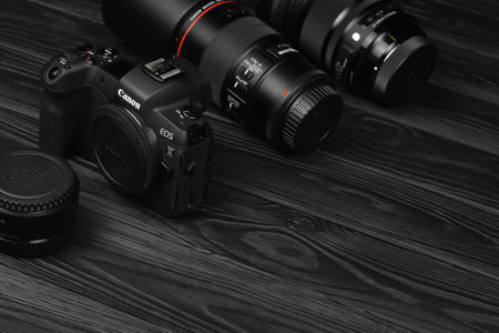 KHARKOV, UKRAINE - NOVEMBER 23, 2020: Canon EOS R photocamera and mount adapter EF - EOS R with Canon 105mm f2.8 and Sigma 24-105 f4 Art lenses on black wooden tableのeditorial素材