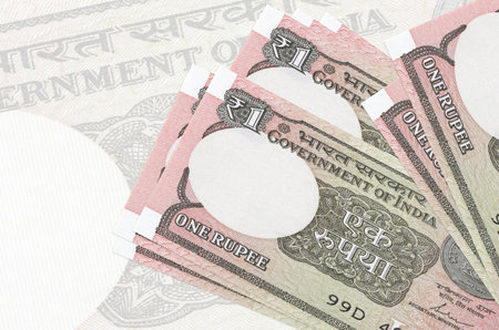 1 Indian rupee bills lies in stack on background of big semi-transparent banknote. Abstract...