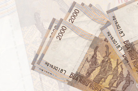 2000 Indonesian rupiah bills lies in stack on background of big semi-transparent banknote. Abstract...