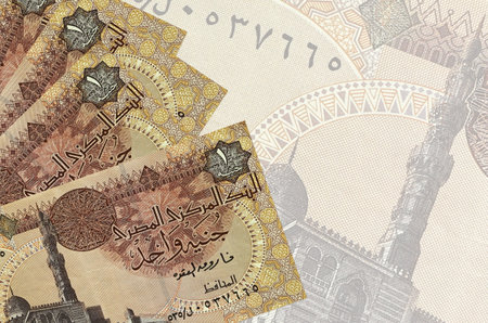 1 Egyptian pound bills lies in stack on background of big semi-transparent banknote. Abstract...