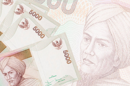 5000 Indonesian rupiah bills lies in stack on background of big semi-transparent banknote. Abstract...