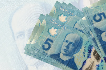 5 Canadian dollars bills lies in stack on background of big semi-transparent banknote. Abstract presentation of national currency. Business conceptの写真素材