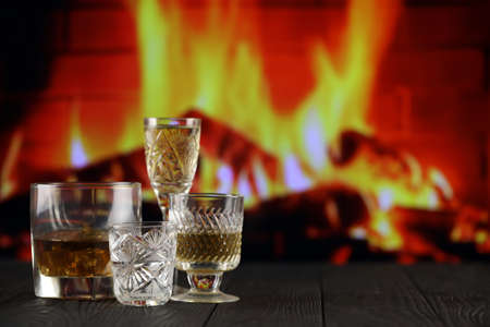 Different alcohol drinks in glass on wooden surface on fireplace background. Luxury elite alcohol in glass cups. Low key dark sceneの写真素材
