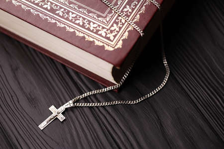Silver necklace with crucifix cross on christian holy bible book on black wooden table. Asking blessings from God with the power of holiness, which brings luck and shows forgiveness.の写真素材