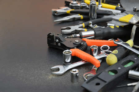 Handyman tool kit on black wooden table. Many wrenches and screwdrivers, pilers and other tools for...