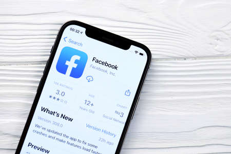 KHARKOV, UKRAINE - MARCH 5, 2021: Facebook icon and application from App store on iPhone 12 pro display screen on white wooden tableのeditorial素材