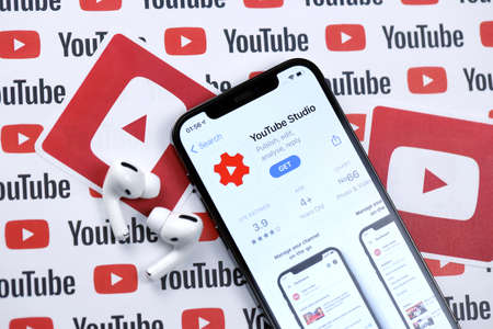 KHARKOV, UKRAINE - MARCH 5, 2021: Youtube studio icon and application from App store on iPhone 12 pro display screen with airpods pro on white wooden tableのeditorial素材