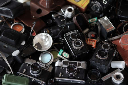 KHARKOV, UKRAINE - APRIL 27, 2021: Film photo cameras and another old retro photo equipment on black wooden table in photographer darkroom. Photographic gear from soviet union timesのeditorial素材