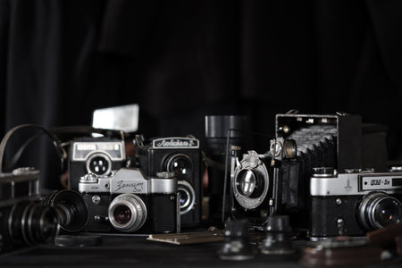 KHARKOV, UKRAINE - APRIL 27, 2021: Film photo cameras and another old retro photo equipment on black wooden table in photographer darkroom. Photographic gear from soviet union timesのeditorial素材