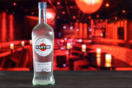 KHARKOV, UKRAINE - FEBRUARY 14, 2021: Martini e Rossi blanco bottle on wooden table with red bar interior on background. Elite alcohol productionのeditorial素材