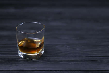 Glass with cognac or whiskey alcohol drink on black wooden table close up with copy space for text. Luxury elite alcohol drinking or alcoholism conceptのeditorial素材