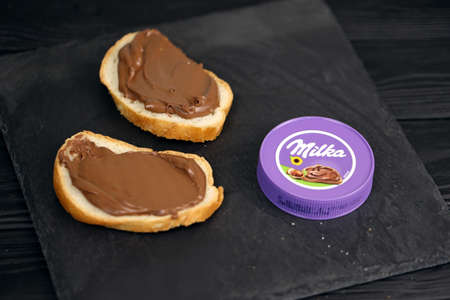 KHARKOV, UKRAINE - JULY 2, 2021: Milka sweetened hazelnut cocoa spread with classical lilac color design on black wooden tableのeditorial素材