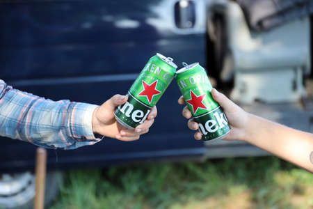 KHARKOV, UKRAINE - JULY 31, 2021: Green tin cans of Heineken pale lager beer in men hands outdoors