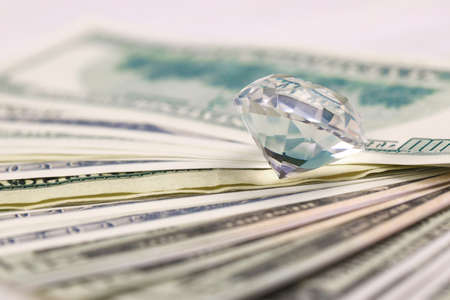 US money bills with large diamond close up. Big amount of dollars and huge transparent gem on table....