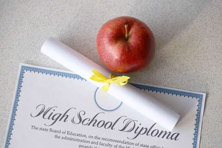 A high school diploma lies on table with small scroll and red apple. Education documents close upの写真素材