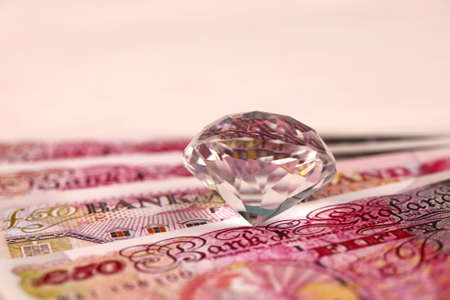 UK money bills with large diamond close up. Big amount of United Kingdom pounds and huge transparent gem on table. Business and jewelery concept for Englandの写真素材