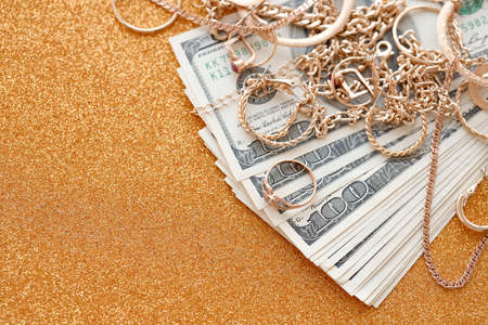 Many expensive golden jewerly rings, earrings and necklaces with big amount of US dollar bills on luxury glitter golden background surface. Pawnshop or jewelery shop conceptの写真素材
