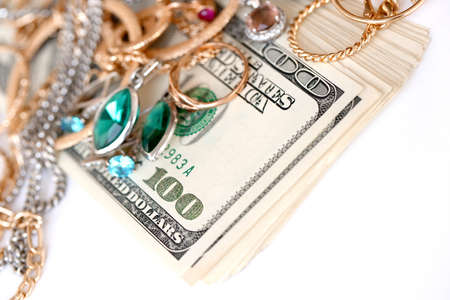 Many expensive golden and silver jewerly rings, earrings and necklaces with big amount of US dollar bills on white background. Pawnshop or jewelery shop conceptの写真素材