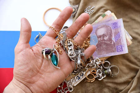 Marauders hand with a bunch of stolen jewelry and money on military uniform cloth fabric and Russian...
