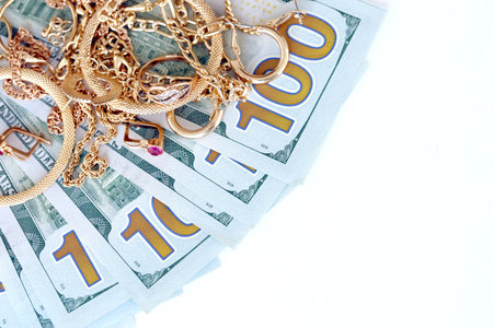 Many expensive golden jewerly rings, earrings and necklaces with big amount of US dollar bills on white background. Pawnshop or jewelery shop conceptの写真素材